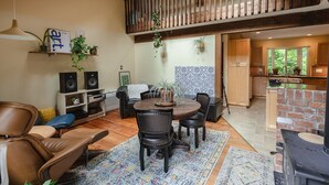 A spacious living area with a dining table, leather chairs, a fireplace, and a kitchen in the background. - Rustic & Serene Forest 4 Bedroom Home - West Coast Retreat (Willis Point)