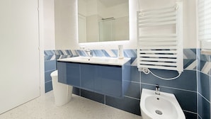 A bathroom with a white sink, a mirror, a bidet, and a trash bin.
