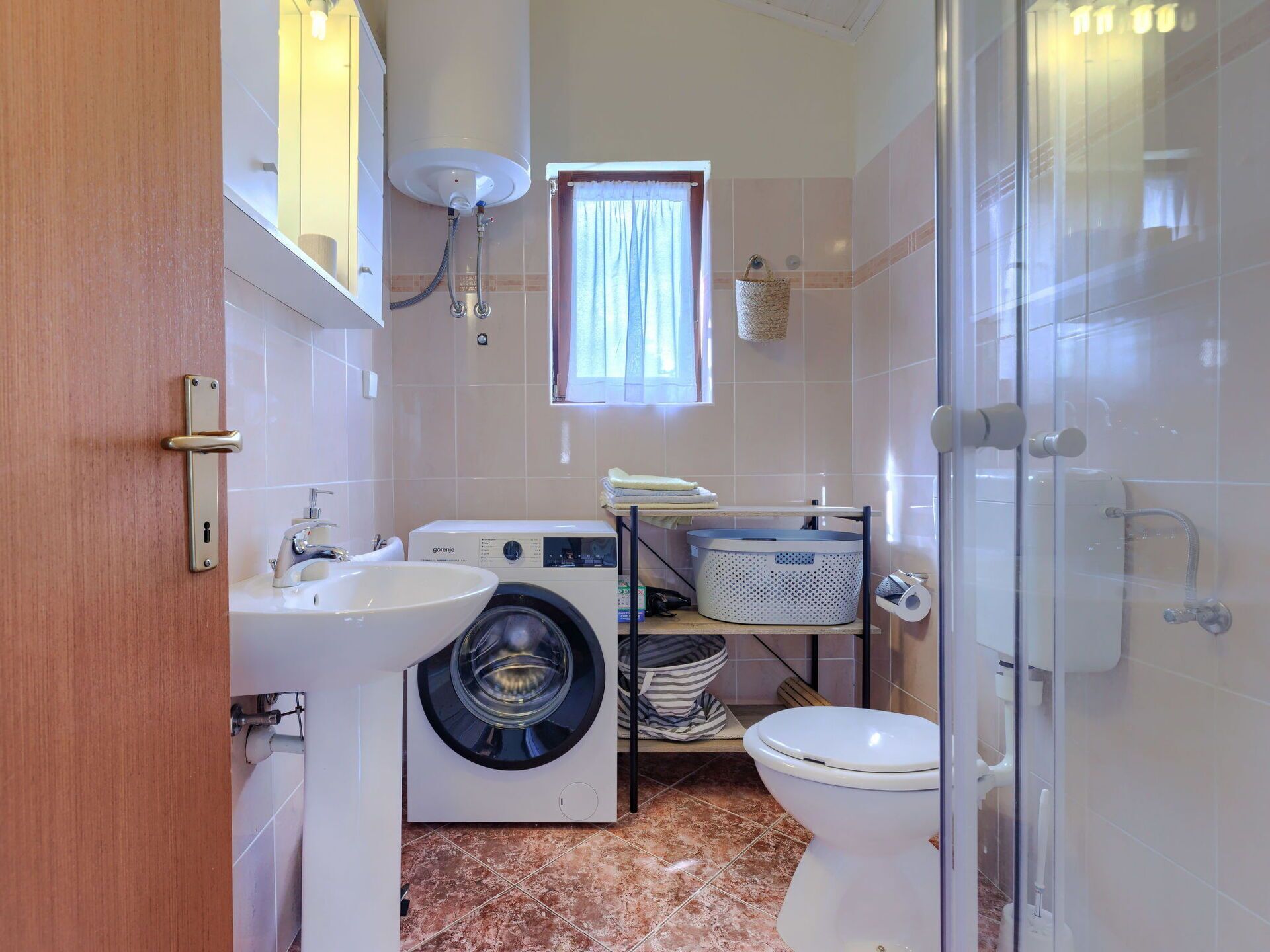 A compact bathroom with a washing machine, a sink, a toilet, and a shower area.