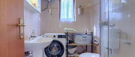 A compact bathroom with a washing machine, a sink, a toilet, and a shower area.