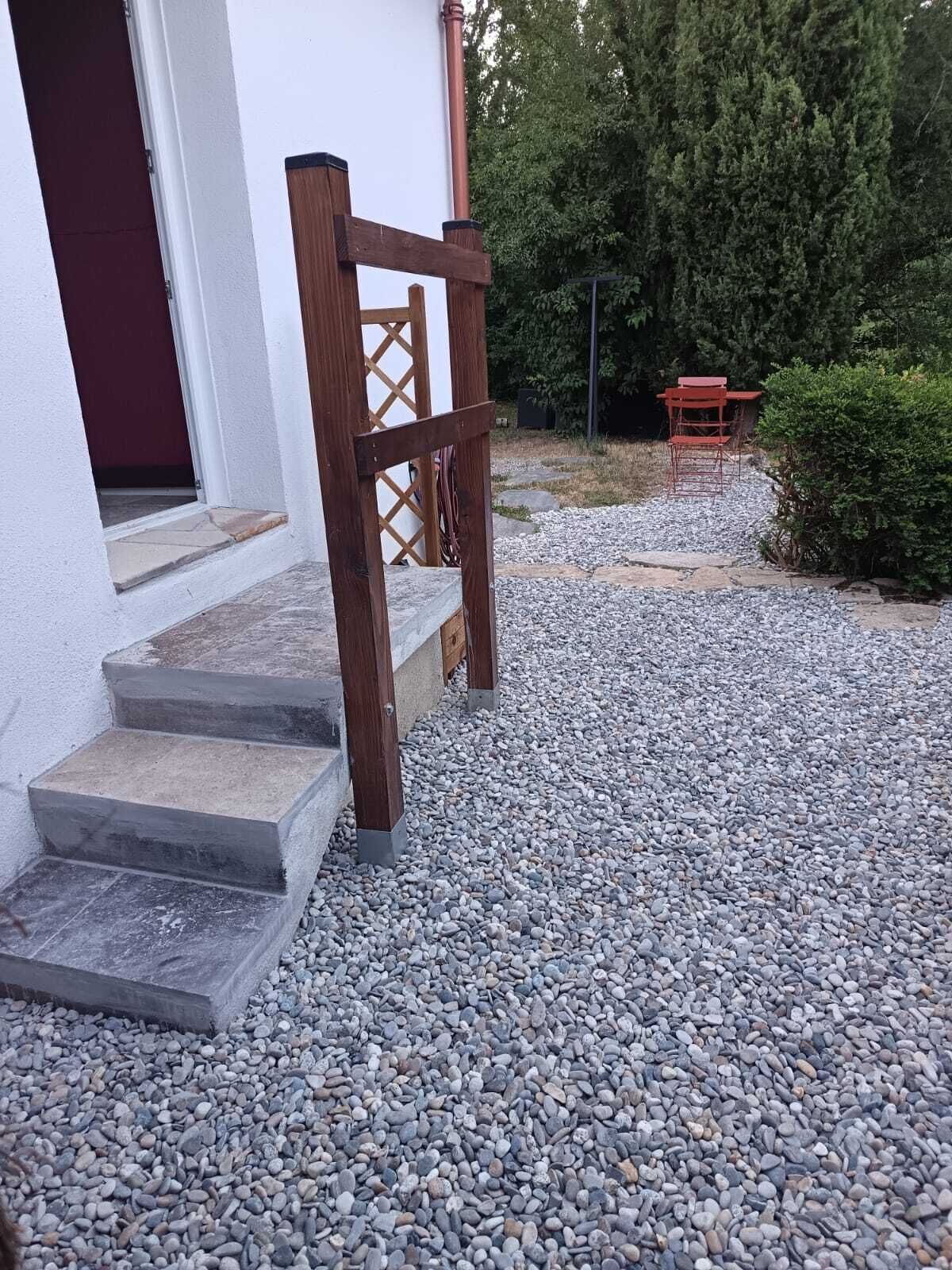 Un escalier en pierre menant à une porte en bois, un chemin de gravier et une chaise rouge dans un jardin.