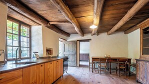 Une cuisine rustique avec des poutres en bois, un grand îlot central doté d’un évier et un coin repas avec des chaises.
