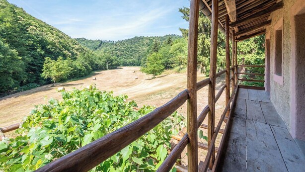 Un balcon en bois offrant une vue sur une vallée verdoyante et des collines.