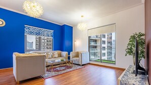 Un salon moderne avec un mur d’accent bleu, deux canapés, une table basse et une grande fenêtre donnant sur la ville.