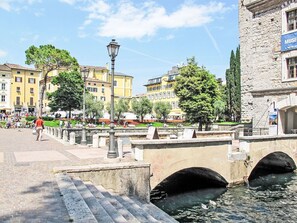 Eine historische Brücke mit steinernen Bögen über einem Kanal, umgeben von Bäumen und Gebäuden mit klassischer Architektur.