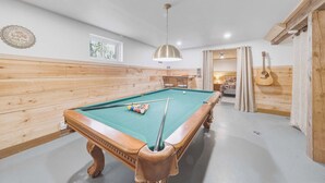 A pool table with balls, a hanging light fixture, wooden walls, and a guitar.