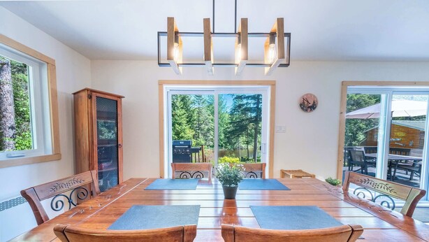 A dining area with a wooden table, chairs, a chandelier, and large windows.