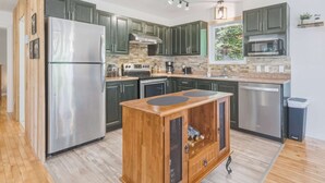 A modern kitchen with dark green cabinets, stainless steel appliances, and a wooden cabinet with a mesh front.