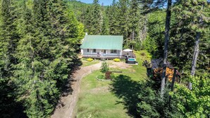 A cabin surrounded by dense forest, with a visible deck and a clear sky.