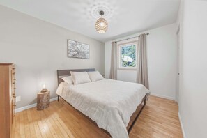 Une chambre à coucher comprenant un lit, une lampe de chevet, une fenêtre avec des rideaux et une œuvre d’art accrochée au mur.