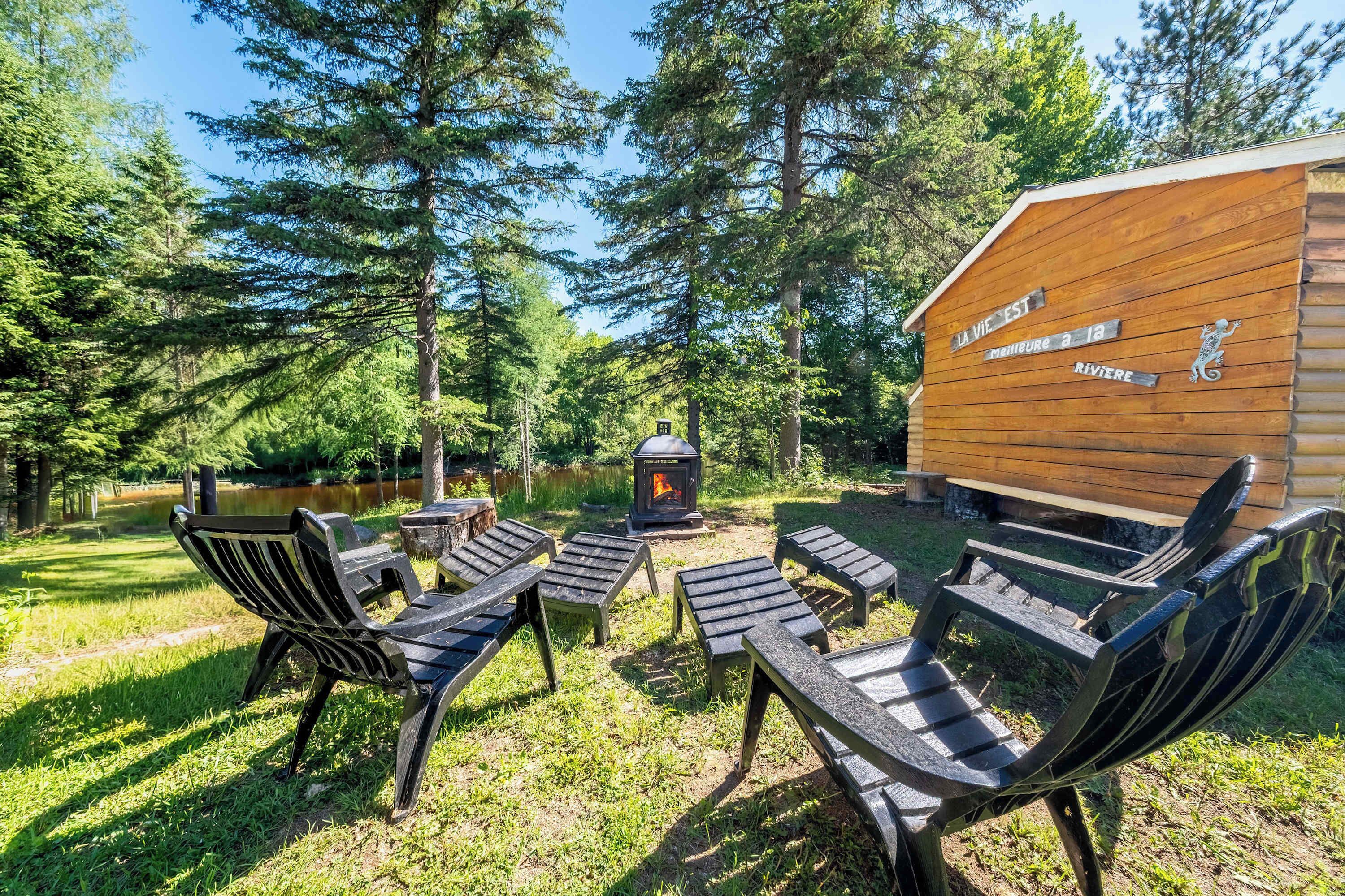 Una cabaña con fogata, asientos exteriores y un letrero que dice 'La Vie Est' y 'Meilleure à la Rivière'.