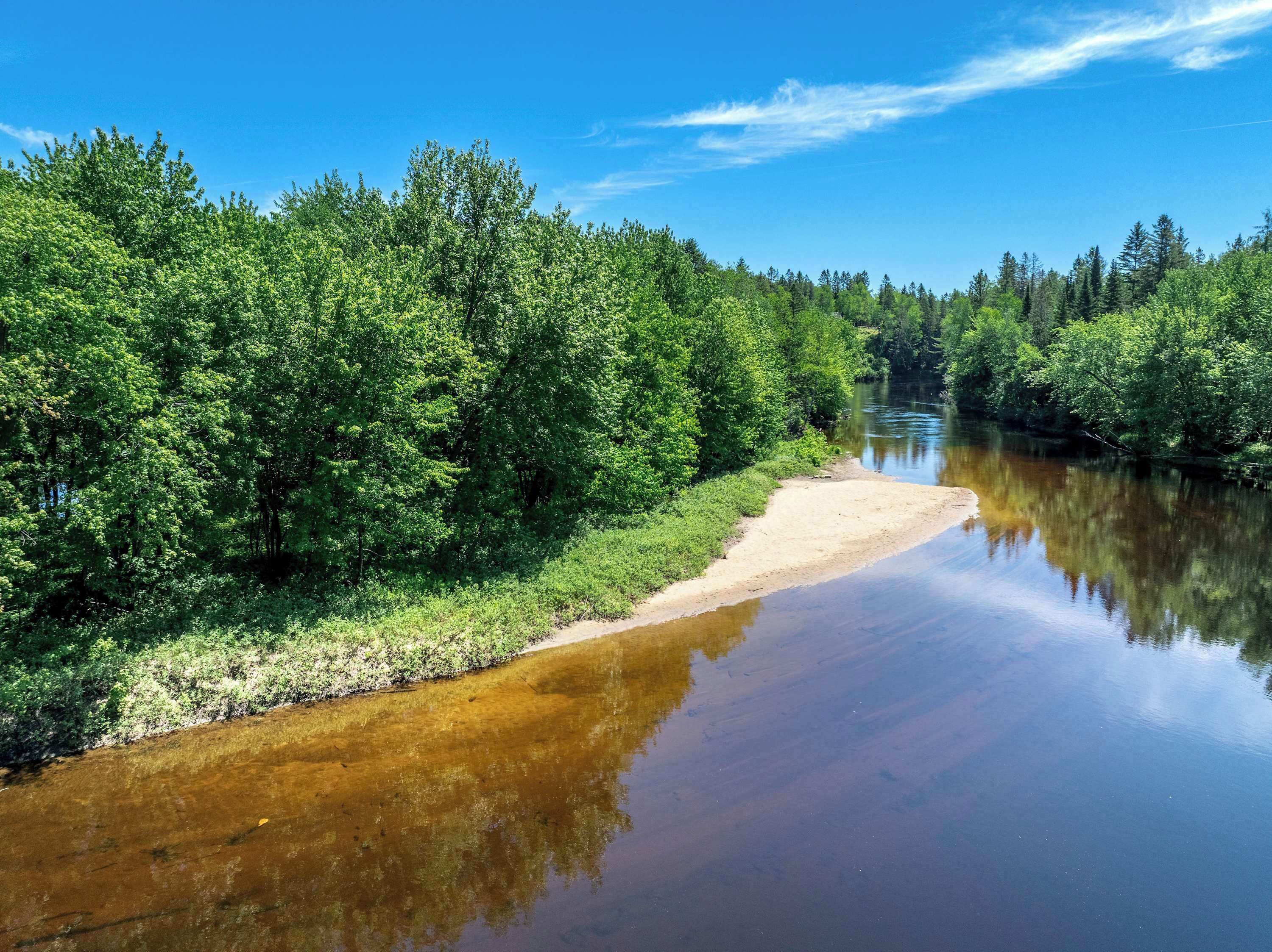 Une rivière bordée de part et d’autre d’une végétation luxuriante et verdoyante, dont les eaux reflètent le ciel.