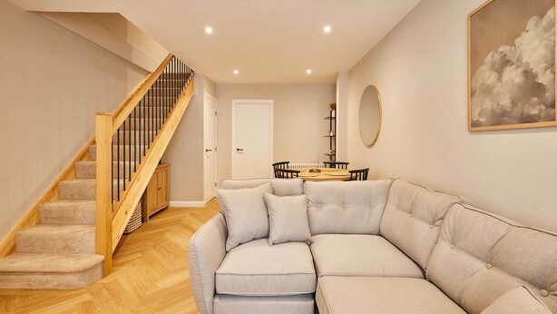 A living room with a beige sectional sofa, a wooden staircase, and a dining area with a round table. - Host & Stay | Belvedere Terrace (Scarborough)