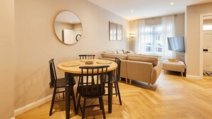 A modern living room with a round dining table, chairs, a sofa, a TV, and a large mirror on the wall. - Host & Stay | Belvedere Terrace (Scarborough)