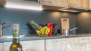 Una cucina moderna con mobili in legno, un lavandino in acciaio inossidabile, una ciotola di frutta, un elettrodomestico rosso e un tagliere.