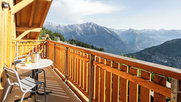 Een houten balkon met een tafel en stoelen, met uitzicht op een bergachtig landschap.