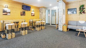 Een kamer met houten wanden, een grijs tapijt, houten krukken, een grijze bank en een aan de muur bevestigde televisie.