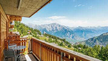 Un balcon en bois, agrémenté d’une table et de chaises, qui offre une vue sur un paysage montagneux.