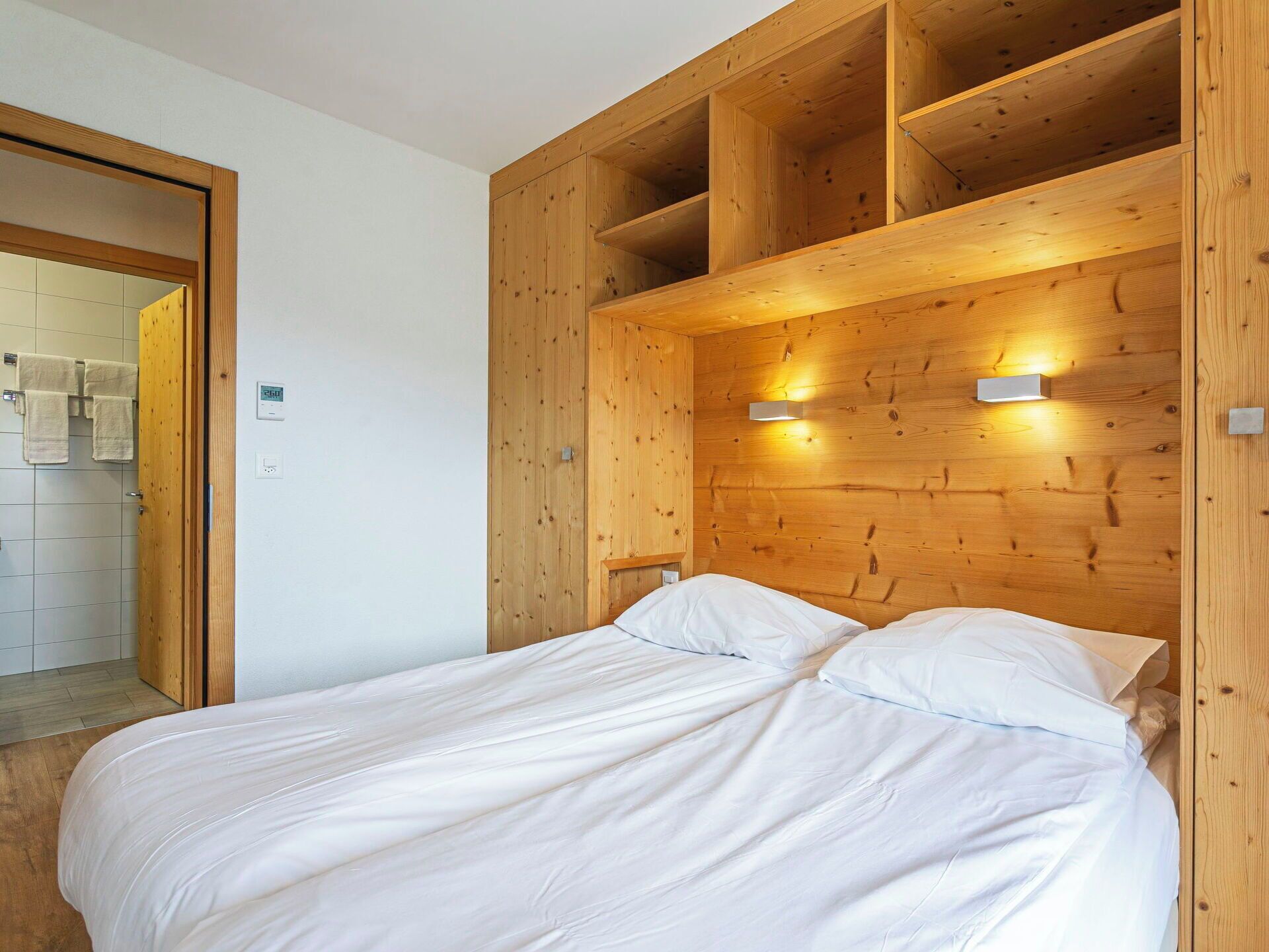 Une chambre à coucher avec une tête de lit en bois, un lit avec une literie blanche et deux appliques murales.
