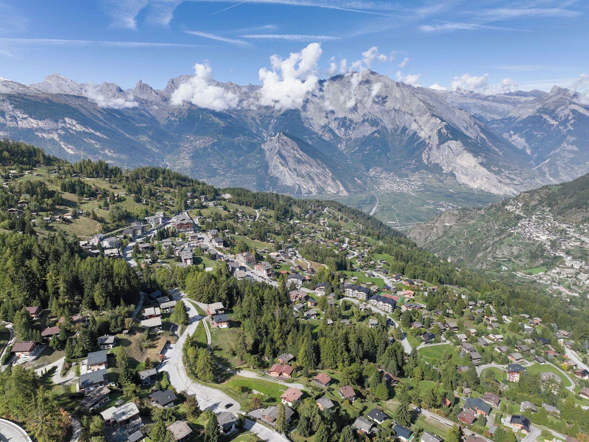 Ein dorfähnliches Bergstädtchen mit Häusern, umgeben von Grünflächen und Bergen im Hintergrund.