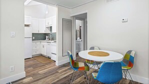 Een moderne keuken met witte kastjes, een backsplash in visgraatmotief, en een eetgedeelte met een ronde tafel en kleurrijke stoelen.