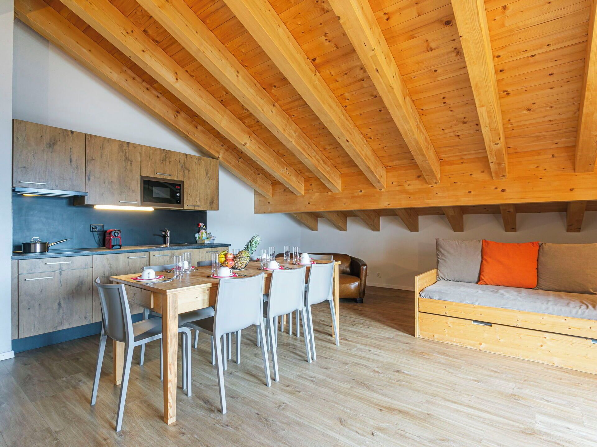 Une cuisine moderne avec des poutres en bois, un coin repas avec une table et des chaises, et un canapé avec des coussins.