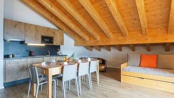 Une cuisine moderne avec des poutres en bois, un coin repas avec une table et des chaises, et un canapé avec des coussins.
