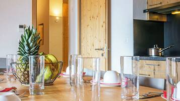 Une table à manger en bois, avec des verres transparents, un ananas et un panier de fruits.