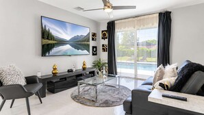 En moderne stue med et fladskærms-TV, et glasbord, en sofa og udsigt til en pool.