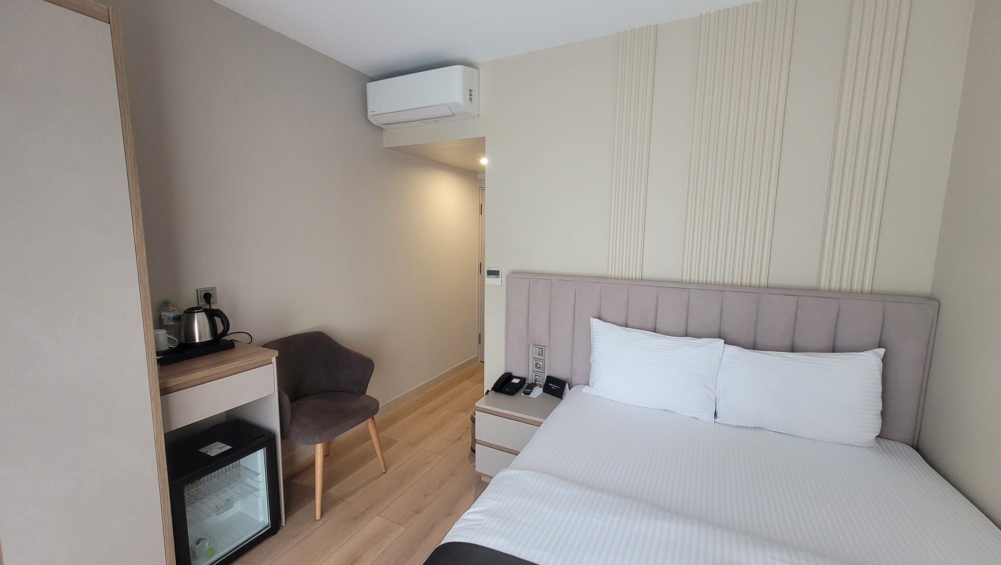 Habitación de hotel con cama, mesita de noche, silla y una pequeña cocina.