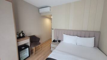Habitación de hotel con cama, mesita de noche, silla y una pequeña cocina.