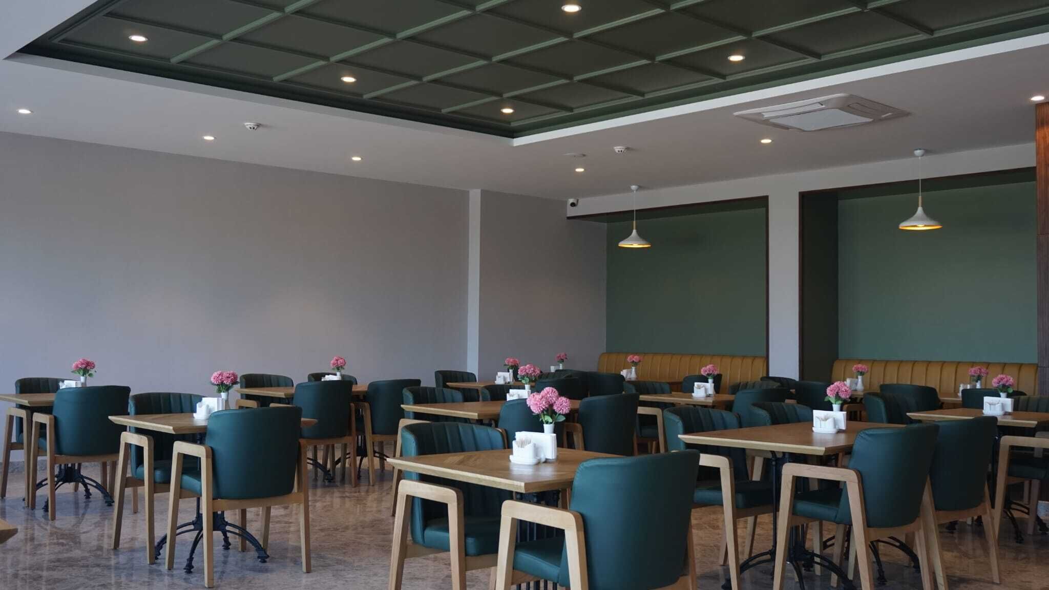 A conference room with multiple tables and chairs, equipped with ceiling lights and a large screen.