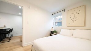A bedroom with a bed, a desk with chairs, a window, and a wall-mounted artwork. - Modern 1BR in the Heart of Ottawa (Ottawa)