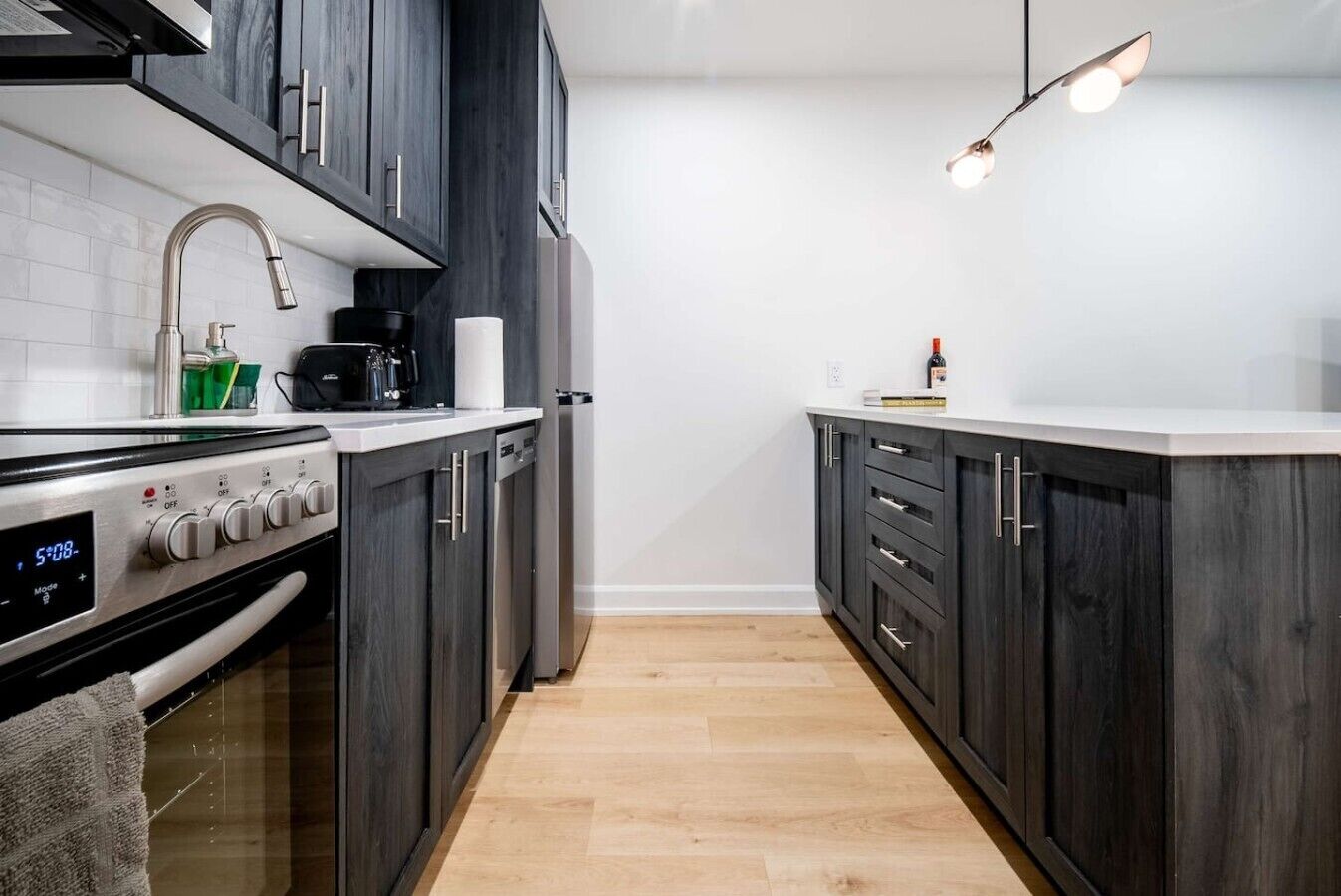 Una cocina moderna con armarios de madera oscura, estufa de acero inoxidable y un reloj digital.