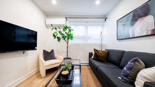 A modern living room with a sofa, armchair, coffee table, TV, and a large window. - Modern 1BR in the Heart of Ottawa (Ottawa)