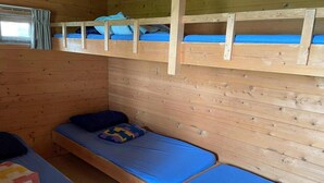 Eine Holzhütte mit zwei Etagenbetten und einem Einzelbett, Holzwänden und einem Fenster mit Vorhängen.