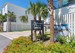A sign for Pelican Place Cottages with a modern building in the background. - Heated Pool Access | Sleeps 10 | Steps to Beach (Gulf Shores)