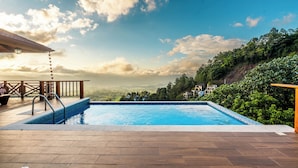 Une piscine dotée d’une terrasse en bois, d’une rambarde et offrant une vue sur une colline.