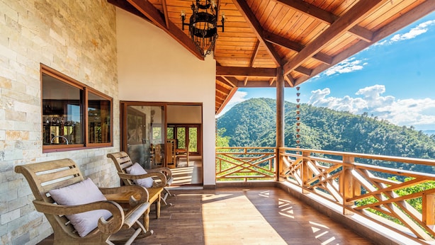 Une terrasse en bois avec des fauteuils à bascule, un mur en pierre et une vue sur un paysage montagneux.