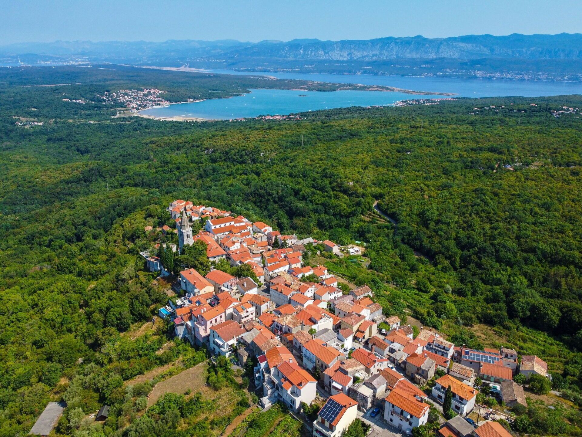 An aerial view of a residential area with houses, a church, and a coastline in the background.