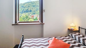 Ein Schlafzimmer mit Fensterblick auf eine grüne Landschaft und einem Bett mit einem gemusterten Überwurf.
