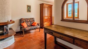Ein Zimmer mit Kamin, einem Holztisch, einer Couch mit orangefarbenen Kissen, einem Holzkasten und einem Fenster mit Blick.