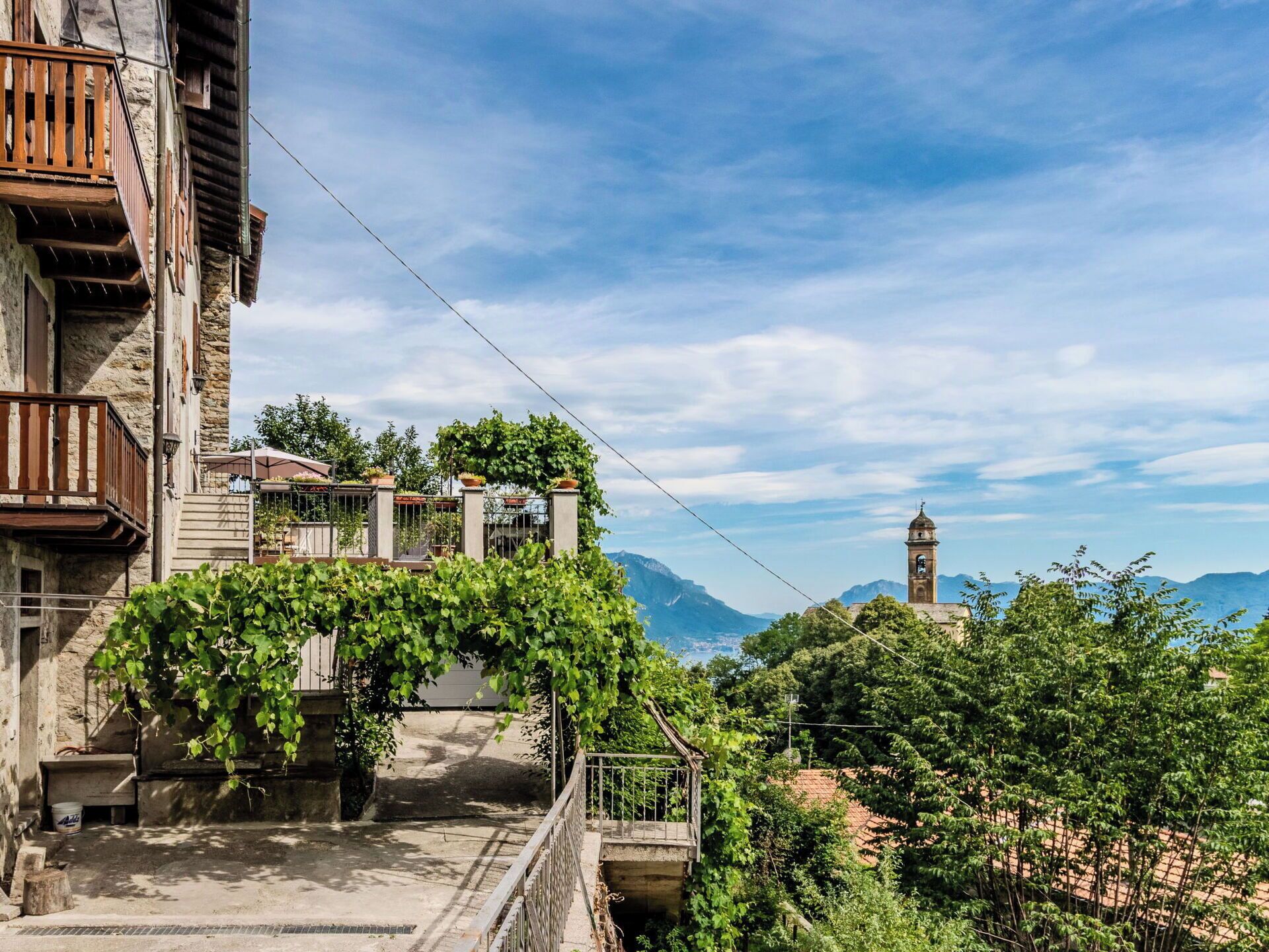 Un bâtiment traditionnel en pierre, doté d’un balcon, offrant une vue sur une montagne et dont on aperçoit un clocher au loin.