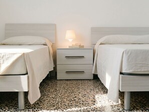 Ein Doppelzimmer mit zwei Betten, einem Nachttisch mit Lampe und Fliesenboden.