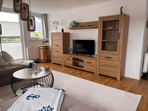 Una sala de estar moderna con un sofá, un televisor, armarios de madera y una mesa de centro redonda.