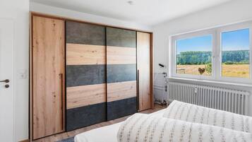Un dormitorio con cama, armario de diseño en madera y color negro, radiador y ventana con vistas a zonas verdes.