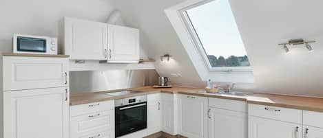 A modern kitchen with white cabinetry, a built-in oven, a microwave, and a window providing natural light.