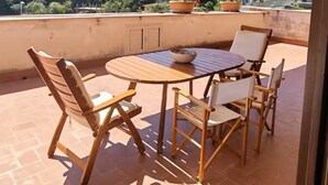 Un balcon avec une table et des chaises, un parasol jaune et une vue sur la verdure et les bâtiments.