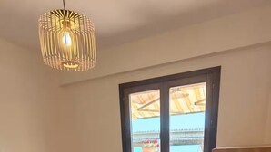 Une chambre à coucher avec un lit, une chaise en bois, une commode rouge et une vue sur l’extérieur, visible à travers une porte.