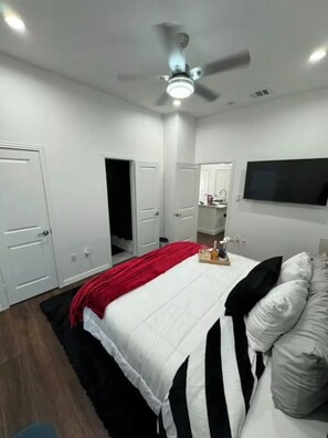 Ein Schlafzimmer mit Bett, Deckenventilator, Fernseher und Spiegel.